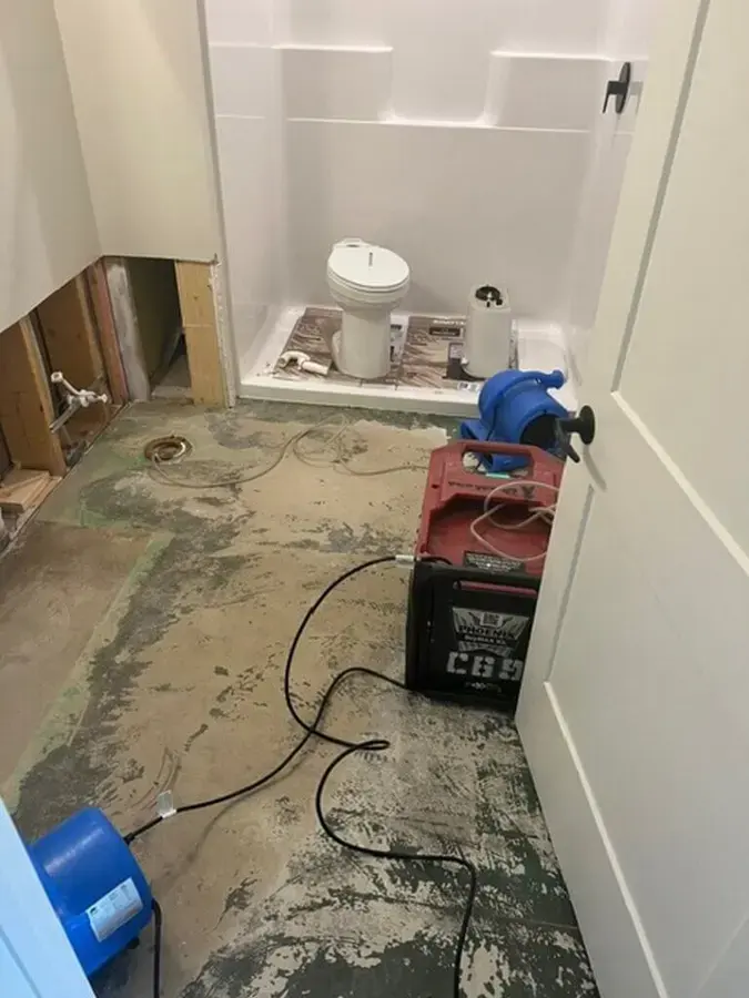 Bathroom opened to the subfloor, a dehumidifier and an air mover set beside the cut tub wall