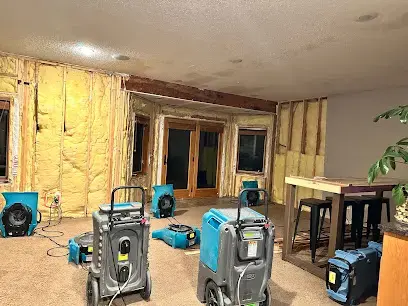 Dehumidifiers and air movers drying a lower-level room with the wall insulation exposed