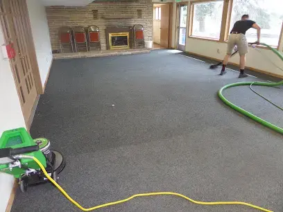 A technician extracting water from living room carpet, the hose trailing out of the room