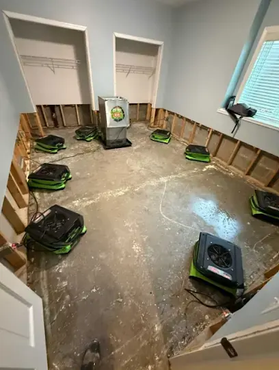 Air movers and a dehumidifier drying a room with the flooring pulled and the wall bottoms cut away
