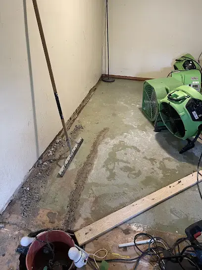 Squeegee pushing water across a wet concrete lower-level floor toward the pit, with air movers set along the wall